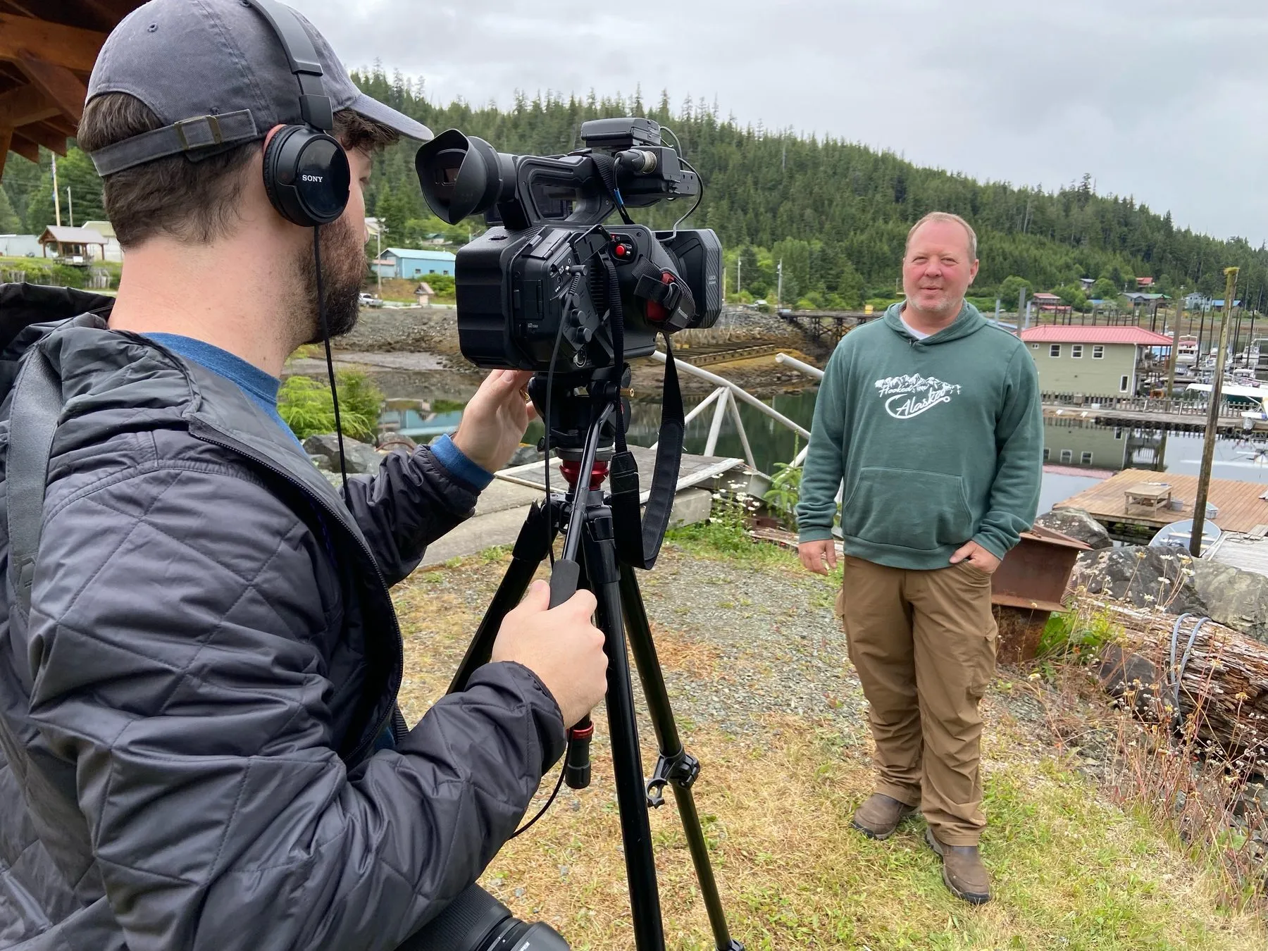 A camera operator filming a man outdoors near the water.